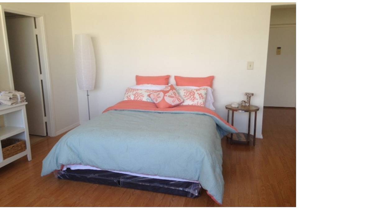 A bed with a blue sheet and pink pillows in a room.